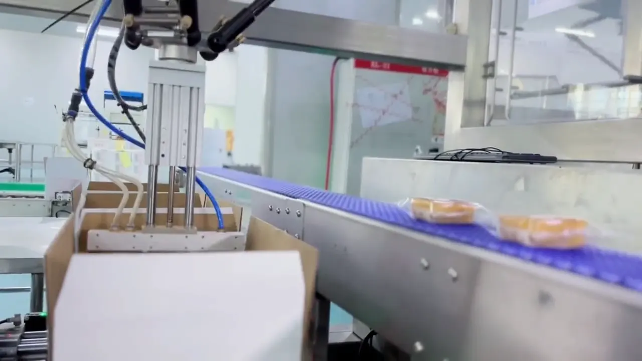 パラレルリンクロボットの吸着ハンドが、コンベヤ上の包装された焼き菓子を取り上げ、箱へ入れる様子