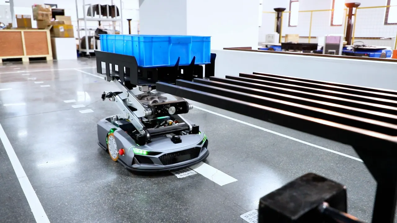 青い樹脂製のコンテナを載せたリフト式のAGV/AMRが、工場内を走行する様子