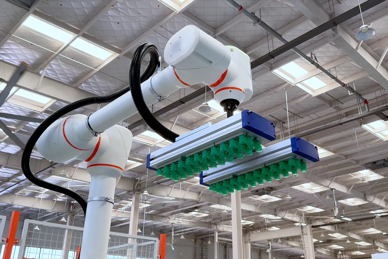 天井の高い工場で、青い吸着ハンドを備えた協働ロボットのアームを見上げる