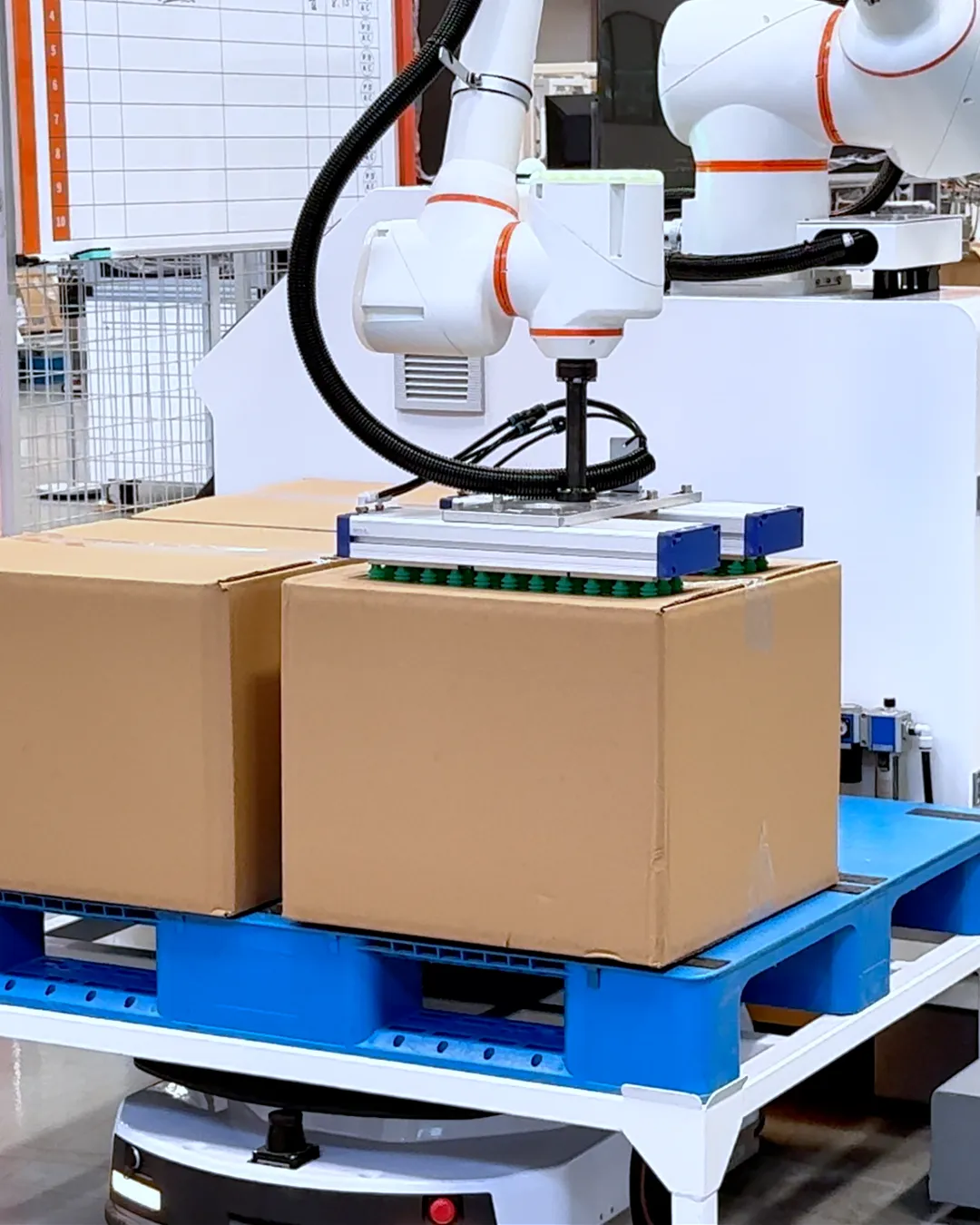 パレットに積んだ段ボール箱の上で、吸着ハンドを構える協働パレタイジングロボット
